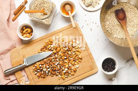 Concetto di cibo sano. Cucinare muesli fatti in casa. Assortimento di noci, farina d'avena, semi e miele su un tavolo in marmo bianco, vista dall'alto. Foto Stock