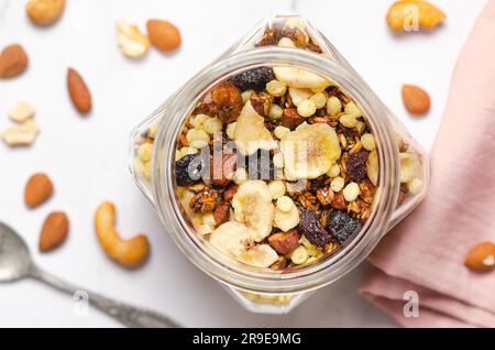 Muesli fatti in casa con fette di banana secche, mirtilli rossi secchi e noci in un vaso di vetro, vista dall'alto. Foto Stock