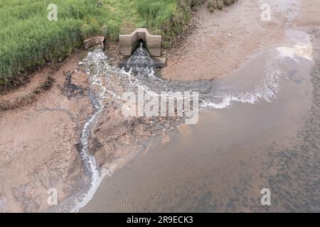 Vista aerea del primo latte (a sinistra) e dello scarico del tubo dell'acqua gallese nell'estuario di Cleddau. La superficie fangosa intertidale è scolorita in rosso a causa del deposito Foto Stock