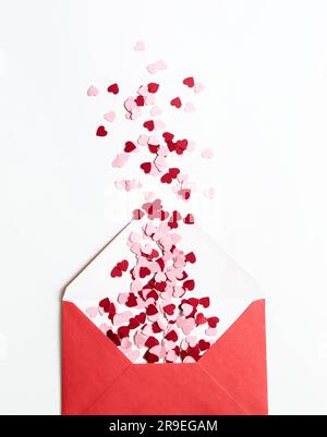 Busta di carta rossa con cuori di valentine rossi e rosa su sfondo bianco. Base piatta, vista dall'alto. Lettera d'amore romantica per il concetto di San Valentino. Foto Stock
