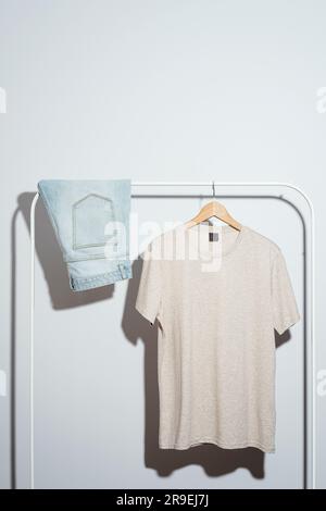 T-shirt beige uomo e pantaloncini denim esposti su appendiabiti bianco. Foto Stock