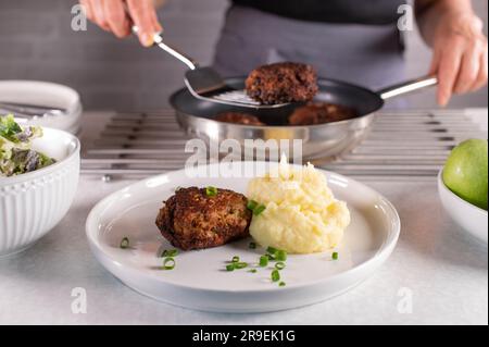 Donna con grembiule che serve polpette da una padella su un piatto Foto Stock