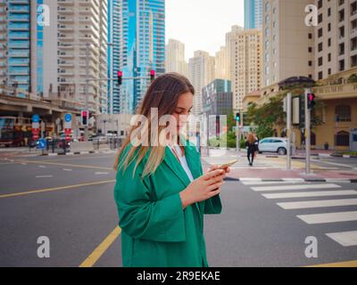 Giovane donna in vestito verde cammina per le strade di Dubai, quartiere di Dubai Marina. Concetto di viaggio negli Emirati Arabi Uniti. l'idea di un expat di successo, trasferirsi in un altro paese, visto di lavoro Foto Stock