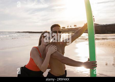 Avventure estive. Allegri giovani surfisti in posa sulla spiaggia al tramonto Foto Stock