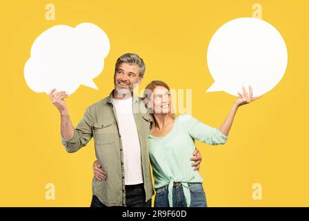 Coppia europea di mezza età con bolle vocali vuote e abbraccianti, posare su sfondo giallo, mockup per il design Foto Stock