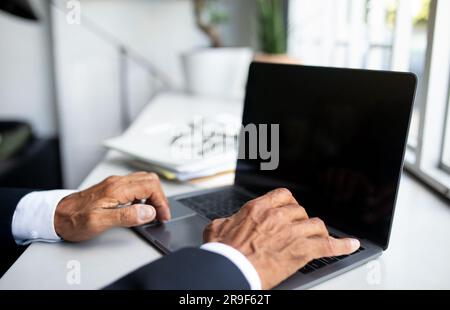 Uomo d'affari europeo maturo in abito che lavora su un computer portatile con schermo vuoto all'interno di un ufficio moderno, ritagliato Foto Stock