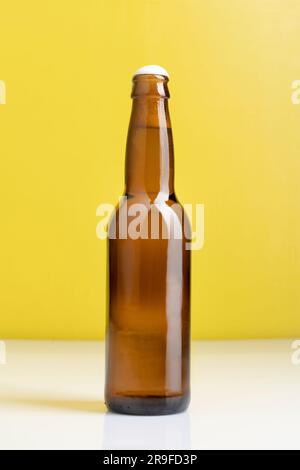 Una bottiglia di birra marrone in piedi su un tavolo bianco su uno sfondo giallo Foto Stock