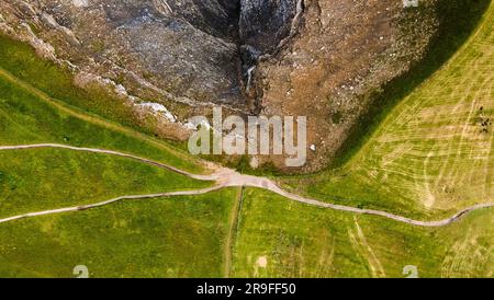 Sali in cima a una cresta di montagna tra i dolemiti con un lato verde con sentieri per passeggiate e un lato roccioso. Fotografia con droni. Colpo di terra. Foto Stock