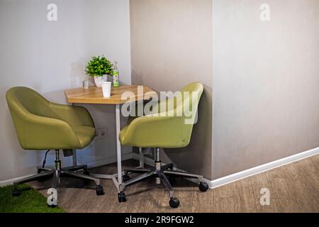 tavolo con sedie verdi da ufficio nell'angolo di una parete di cemento in un moderno interno da ufficio. Area snack per il personale dell'ufficio Foto Stock