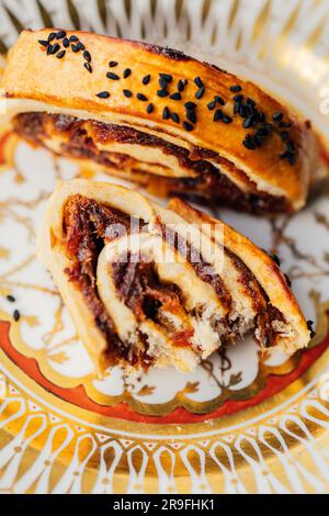 Kleicha, biscotti iracheni in forma di spirale con semi di nigella su un piatto ornato con motivi dorati Foto Stock