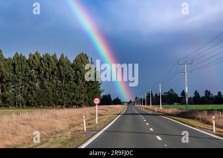 Fotografia di un grande arcobaleno su una strada regionale e un campo agricolo sull'Isola del Sud della nuova Zelanda Foto Stock