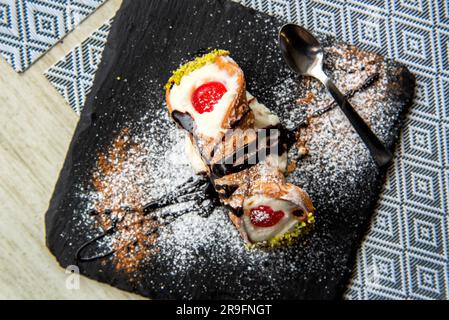 Pasta di cannolo siciliano italiano primo piano su piastra di pietra nera macro con consistenza di crosta gialla e ricotta e crema di pistacchio ripieno Foto Stock