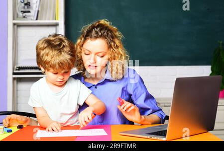 Insegnante femminile di scuola elementare che aiuta il bambino a scrivere lezioni in classe alla scuola elementare. Torna a scuola. Apprendimento e istruzione Foto Stock