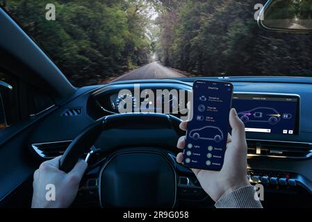 Il conducente utilizza l'app Smart Car durante la guida, per leggere i parametri della vettura. Vista in prima persona della cabina di pilotaggio e dello smartphone in mano Foto Stock