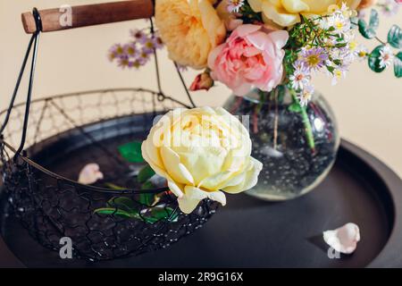Bouquet fresco di fiori di rose messo in vaso di vetro sul tavolo. Primo piano dei fiori rosa-gialli con il cestello. Decorazioni interne Foto Stock