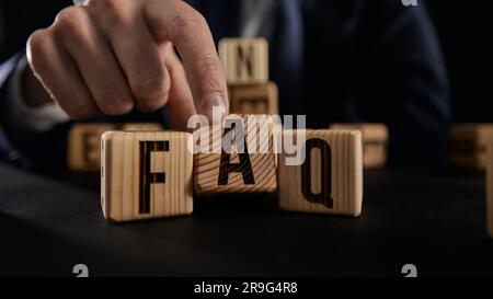 L'uomo d'affari mette blocchi di legno con la parola FAQ. Raccolta di domande frequenti su qualsiasi argomento e relative risposte. Foto Stock