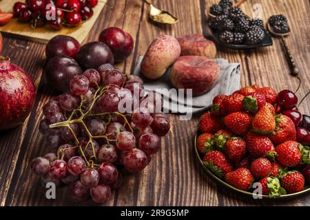 Natura morta con prugne rosse, paraguaiani, uva, bacche, ciliegie mature, su un piatto metallico d'epoca, un mazzo di uva rossa, more scure e un dorso Foto Stock