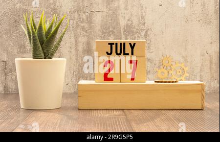Calendario in legno a cubo con data del 27 luglio. Calendario in legno con data sul tavolo. sfoca gli oggetti sullo sfondo. Foto Stock