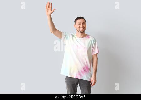 Bell'uomo con t-shirt tie-dye che salta la mano su sfondo chiaro Foto Stock