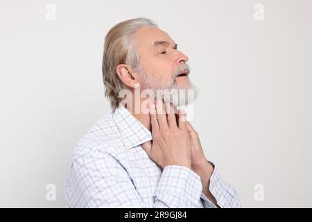 Uomo anziano che soffre di mal di gola su sfondo bianco. Sintomi del freddo Foto Stock