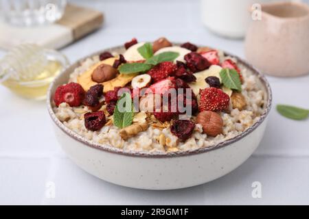 Farina d'avena con frutta secca liofilizzata, noci e menta su un tavolo di legno bianco, primo piano Foto Stock