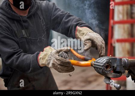 Lavoratore irriconoscibile che utilizza lana d'acciaio sopra un telaio di bicicletta dopo aver passato una torcia elettrica sopra di esso per rimuovere la vernice, come parte del suo lavoro di ristrutturazione bici Foto Stock