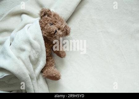 l'orso bruno orsacchiotto si trova avvolto in una coperta bianca morbida, spazio per il testo Foto Stock