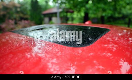 Gocce di pioggia che cadono sul tetto dell'auto rossa. Foto Stock