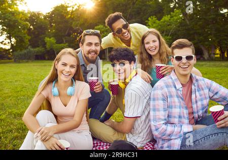 Giovani, allegri e multirazziali, sorridenti durante il picnic, che si divertono e si godono le vacanze estive nel parco Foto Stock