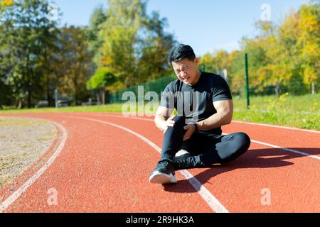 Un corridore si è infortunato alla gamba durante una corsa nel pomeriggio, un uomo asiatico ha un forte spasmo muscolare e dolore alla gamba durante il fitness e l'esercizio attivo, un uomo con una tuta si è infortunato. Foto Stock