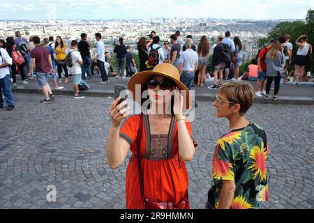 Una donna asiatica alla moda che scatta un selfie a Parigi da Montmartre con i turisti e la vista di dietro mentre un'altra donna indossa una camicia rumorosa Foto Stock