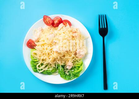 Spaghetti con salmone, formaggio e lattuga su un piatto bianco su sfondo blu Foto Stock