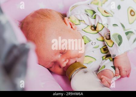 Un neonato beve autonomamente latte o una miscela secca da un biberon, a casa Foto Stock