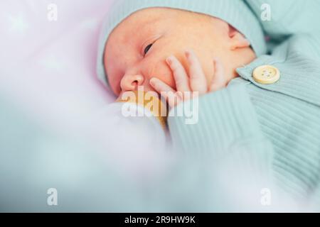 Un neonato beve autonomamente latte o una miscela secca da un biberon, a casa Foto Stock