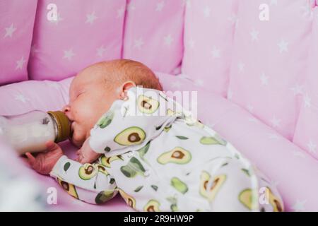 Un neonato beve autonomamente latte o una miscela secca da un biberon, a casa Foto Stock