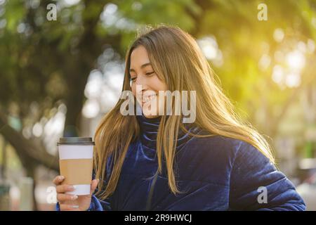 Sorridente bella ragazza latina che beve caffè su una panchina del parco pubblico. Foto Stock