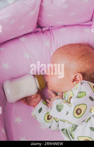 Un neonato beve autonomamente latte o una miscela secca da un biberon, a casa Foto Stock