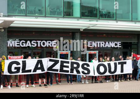 I manifestanti fuori dal campo di calcio del Manchester United chiudono il megastore il giorno in cui il club svela la loro nuova maglia di casa. Striscione testo Glazers Out. Foto Stock