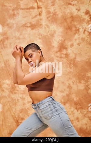 denim fashion, gen z, giovane donna curvy con tatuaggio in posa su sfondo beige macchiato, forme diverse, movimento di positività del corpo, autostima, confondi Foto Stock