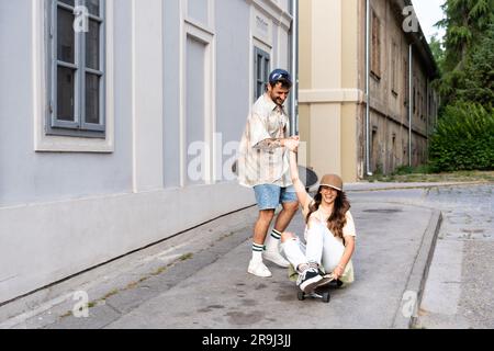 I turisti coppie di skateboarder cavalcano i pattini. Felici i giovani viaggiatori che si imbarcano insieme sul marciapiede al tramonto. Uomo e donna alla moda con un outfit alla moda Foto Stock