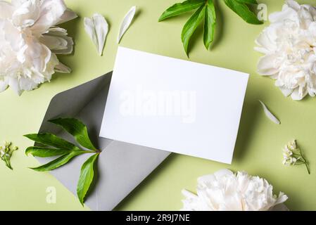Biglietto di auguri o di invito vuoto, fiori di peonia e busta su sfondo verde oliva chiaro, spazio per le copie. Elegante modello creativo, matrimonio romantico Foto Stock