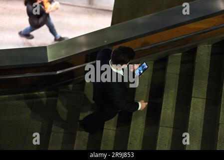 Indossa un uomo d'affari che cammina al piano superiore in un edificio moderno mentre guardi il suo smartphone, visto dall'alto Foto Stock