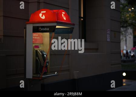 Cabina telefonica pubblica Telstra, con vecchio marchio arancione, accanto a un edificio in città di notte Foto Stock