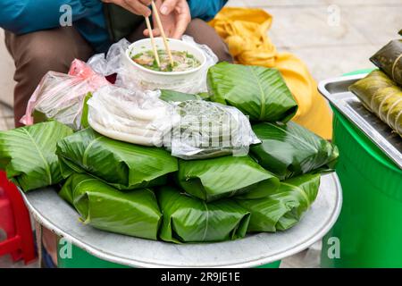 Vista ravvicinata di un vassoio con banh tet o banh chung, che è una torta di riso appiccicosa con una persona seduta accanto al vassoio con una tradizionale ciotola di zuppa Foto Stock