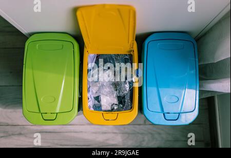 Vista dall'alto dei contenitori di riciclaggio e delle bottiglie di plastica all'interno dei rifiuti di riciclaggio gialli aperti collocati in cucina Foto Stock