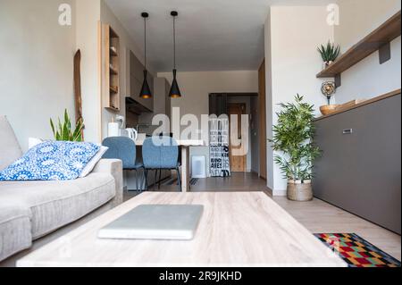 Design interno di un soggiorno minimale con pavimento laminato e pareti bianche che conducono alla zona pranzo mentre sono arredate con comodo divano tavolo centrale Foto Stock