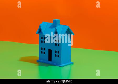 Vista laterale della miniatura blu del modello della casa posizionata su sfondo arancione e verde brillante Foto Stock