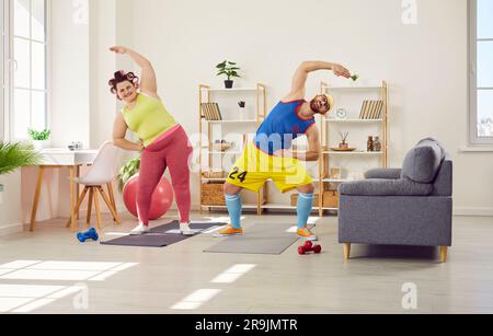 Donna grassa con un uomo barbuto divertente in un brillante abbigliamento sportivo che fa esercizi sportivi a casa insieme. Foto Stock