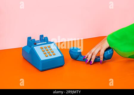 Ritaglia una donna anonima utilizzando un telefono da tavolo cordless giocattolo in plastica rétro su una superficie liscia arancione con sfondo rosa in studio Foto Stock