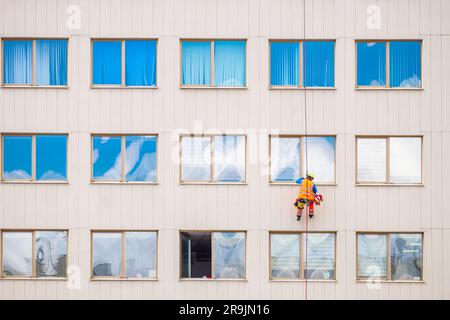 Minsk, Bielorussia - 11 aprile 2022: L'alpinista industriale lava le finestre sulla facciata di un edificio. Vista frontale Foto Stock